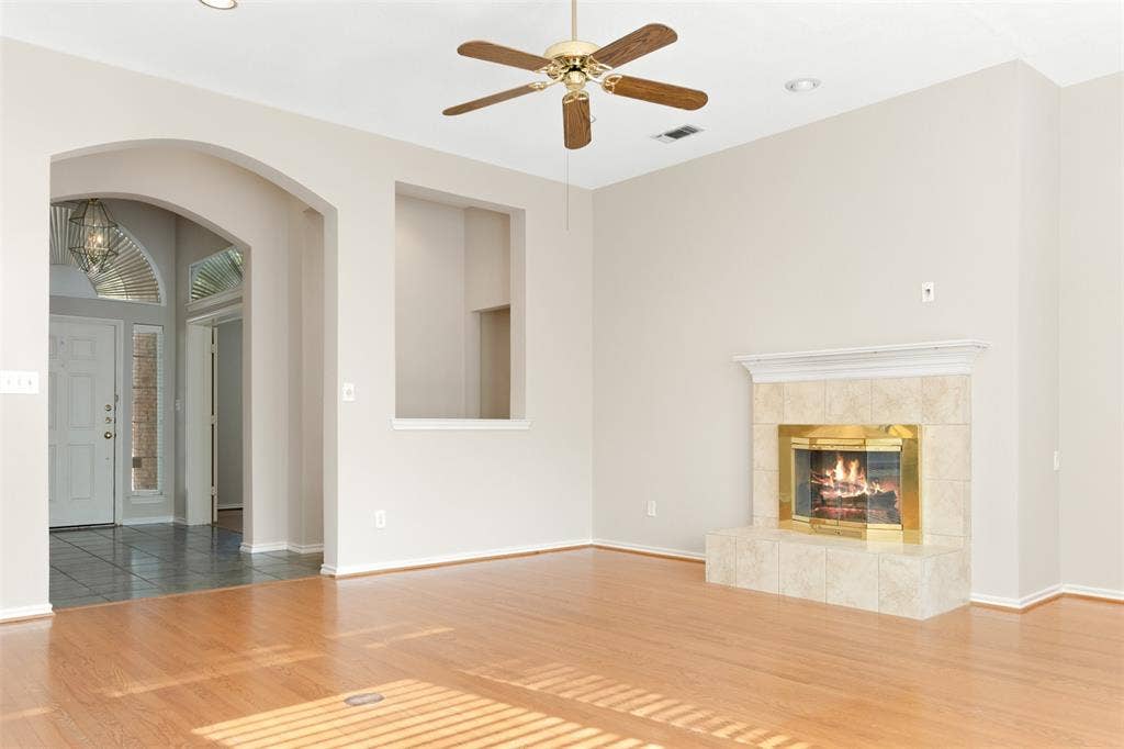 2803 Pheasant Run Drive, McKinney, TX 75072 Living area featuring wood-finish flooring, a recessed wall niche, a fireplace with a neutral-toned tile surround, and an arched entryway