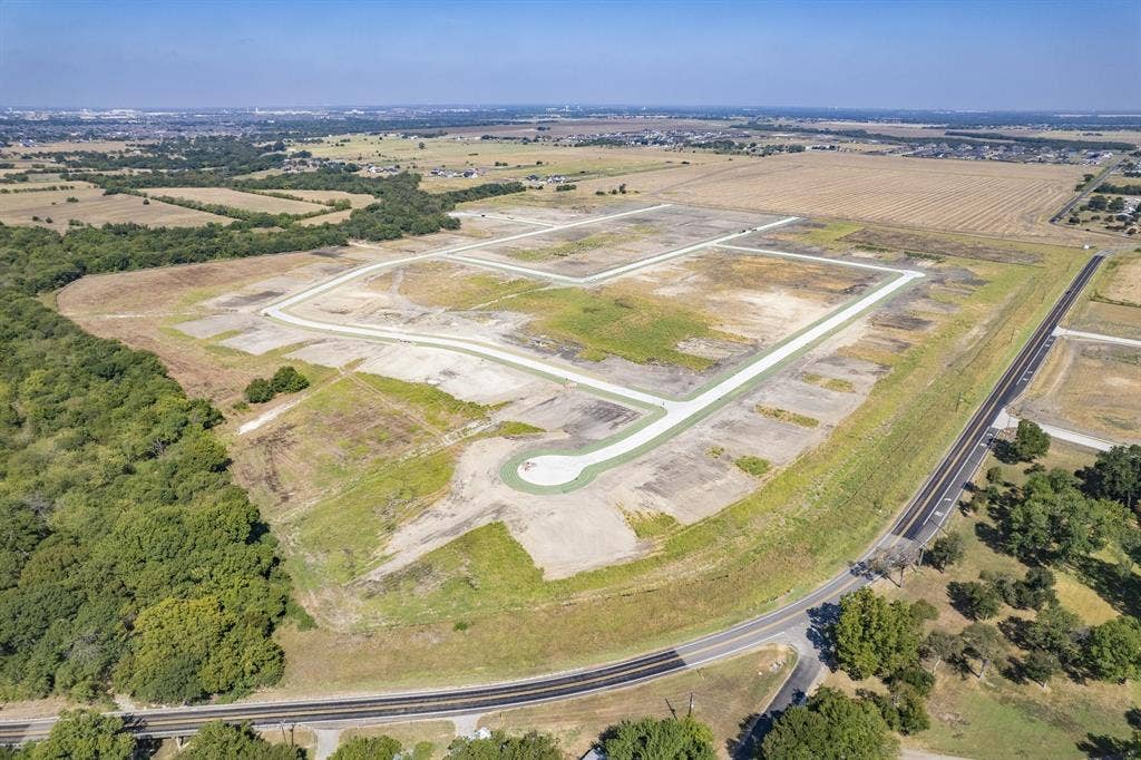 Expansive undeveloped land featuring paved street infrastructure, concrete cul-de-sacs, cleared building pads, and mature perimeter trees