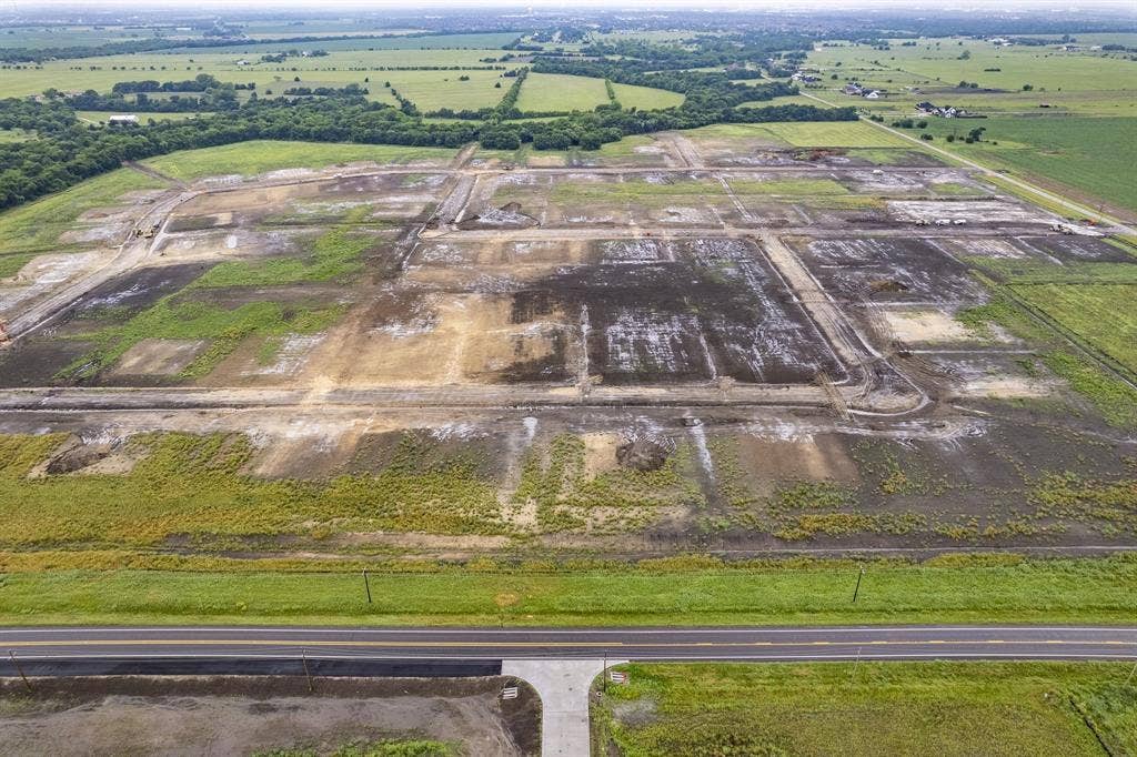 Expansive plot of land featuring cleared building sites, established internal road infrastructure, paved roadway access, and open terrain