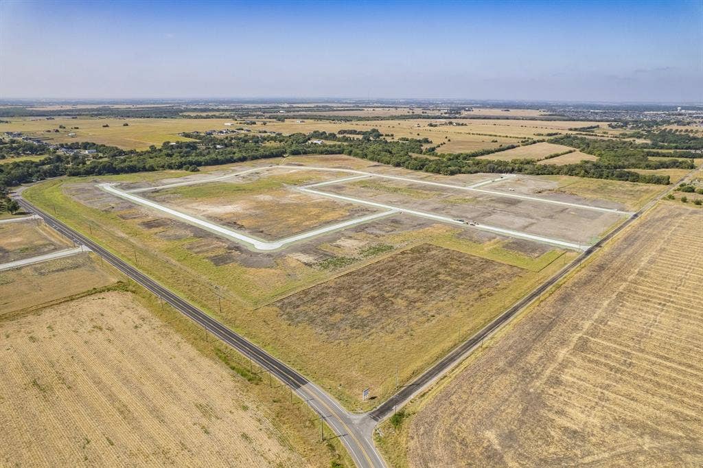 Expansive acreage featuring cleared land, established asphalt road access, and perimeter tree lines