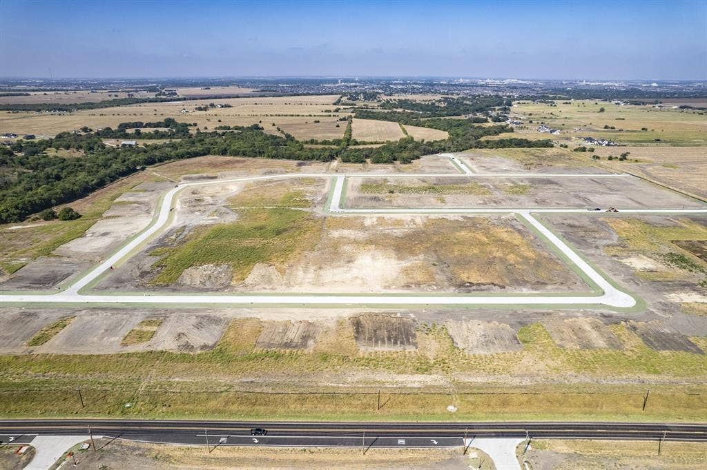 Expansive plot of undeveloped land featuring paved street infrastructure, concrete curbing, and surrounding open terrain