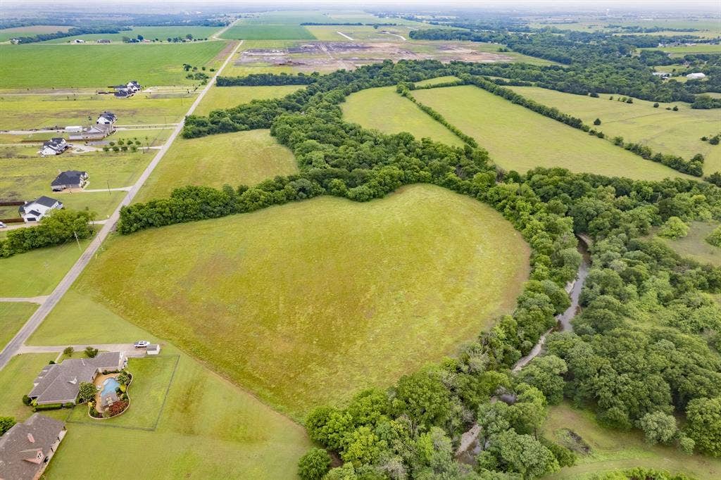 Aerial perspective of expansive acreage featuring open pasture, mature tree clusters, and a natural creek boundary