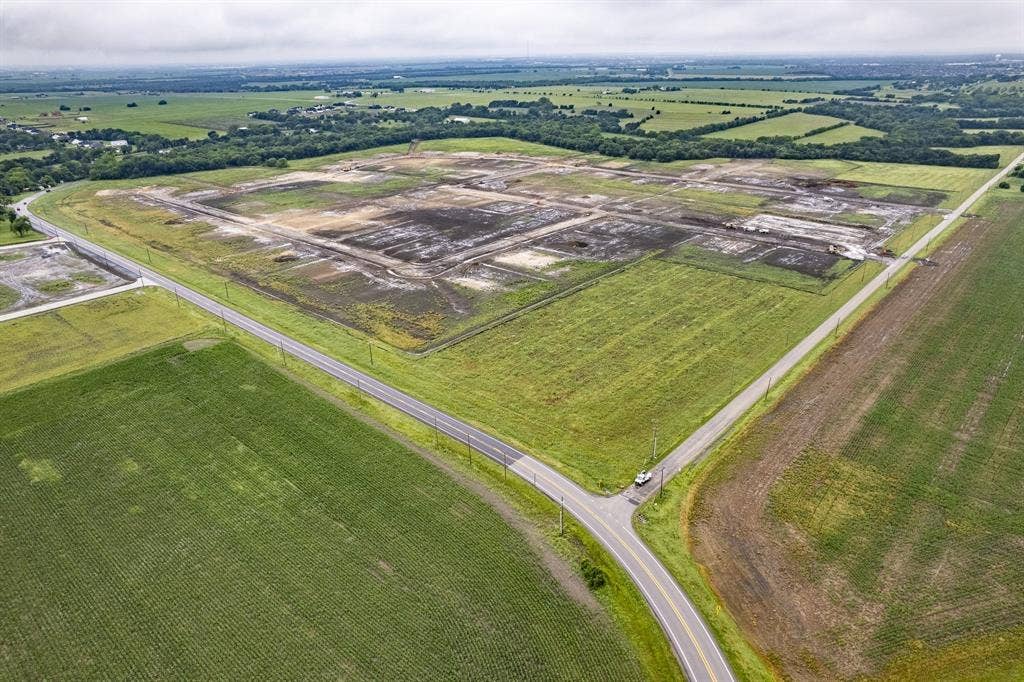 Expansive acreage featuring cleared land, perimeter tree lines, and frontage along two paved roadways