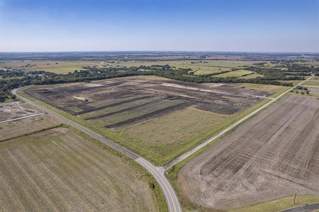 Expansive parcel of cleared land featuring mature perimeter trees, level topography, and dual-road frontage