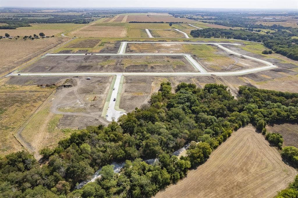 Expansive land parcel featuring established concrete roadway infrastructure, cleared building sites, and dense perimeter tree coverage