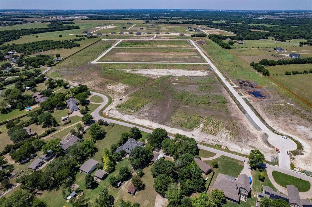 Aerial view of expansive residential acreage featuring cleared development lots, established paved roadway infrastructure, and perimeter tree lines