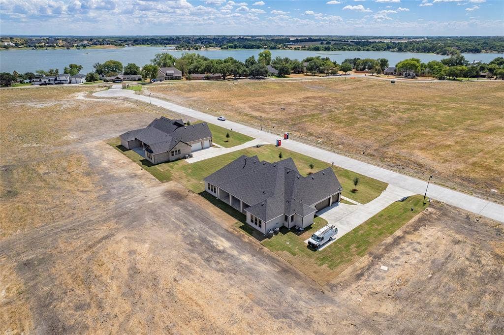 Aerial perspective of a residential property featuring a multi-gabled shingle roof, attached multi-car garage, concrete driveway, and expansive lot