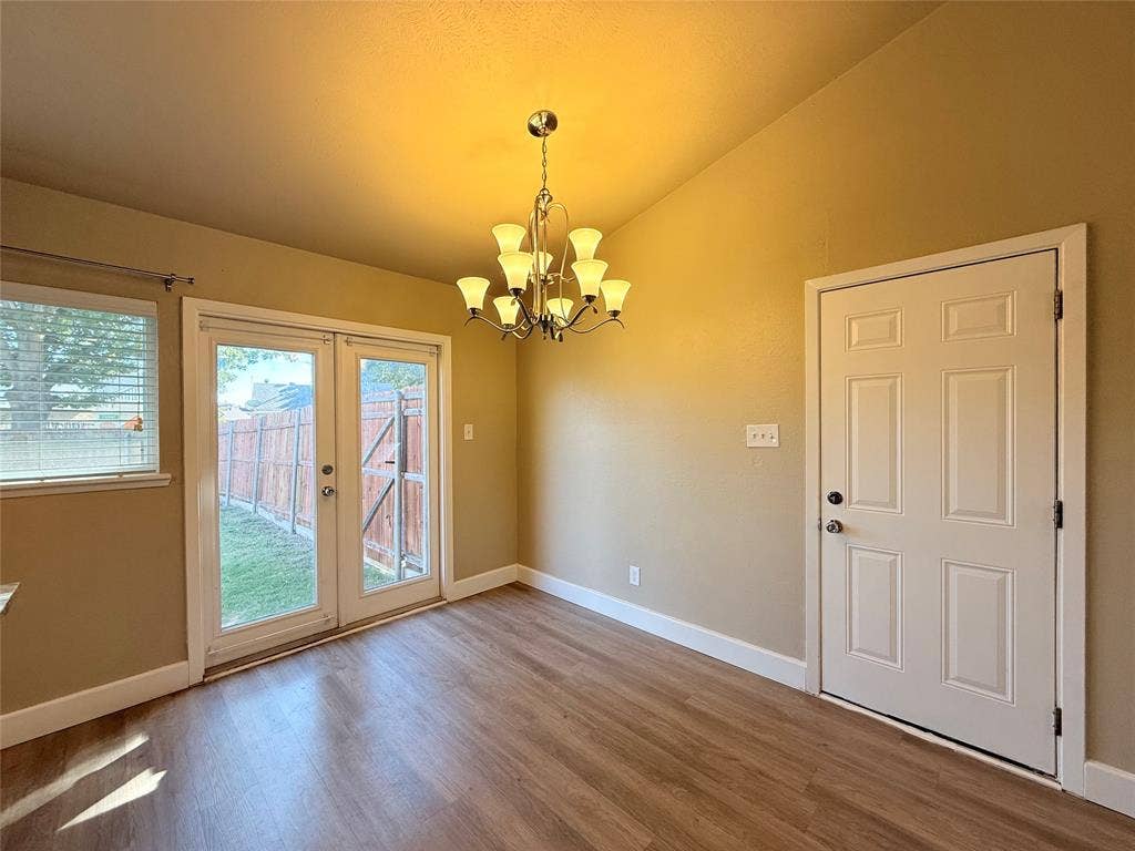 Vaulted ceiling featuring a multi-arm chandelier, wood-finish flooring, dual-pane glass entry door, and six-panel interior door