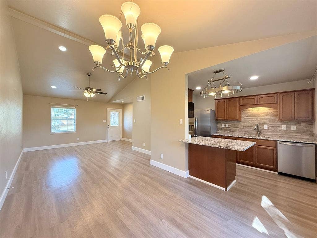 Vaulted ceilings featuring recessed lighting, wood-finish flooring, a multi-arm chandelier, and a kitchen equipped with stone-surface countertops and stainless steel appliances
