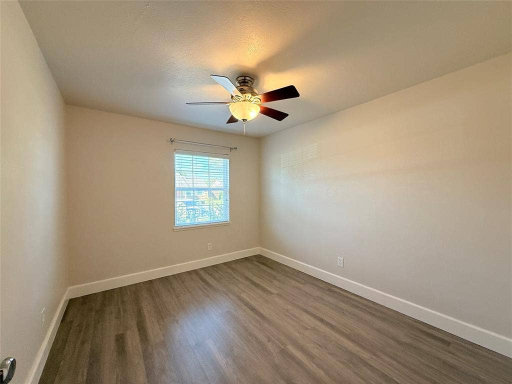 Neutral-toned interior featuring wood-finish flooring, a ceiling fan with integrated lighting, and a single window with horizontal blinds