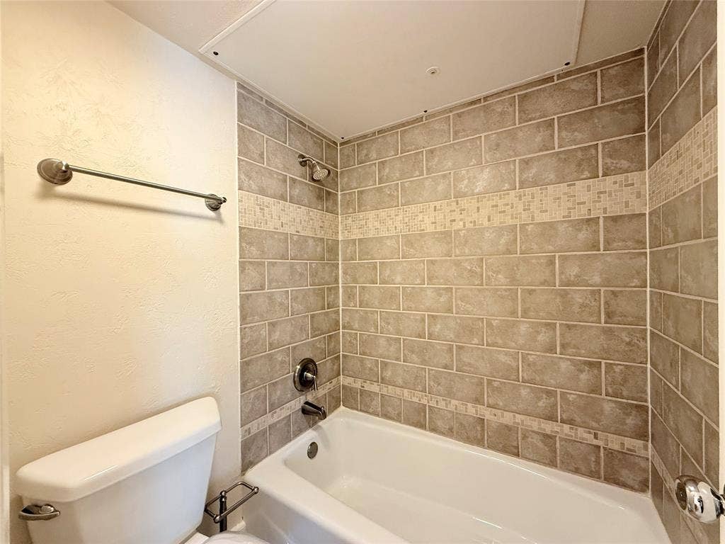 Bathtub with a white surround, integrated shower fixture, and tiled walls featuring a decorative mosaic border inlay