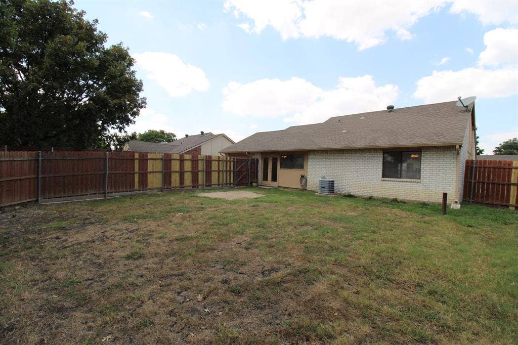 Rear exterior featuring a brick facade, shingle roof, wood privacy fencing, and a concrete patio area