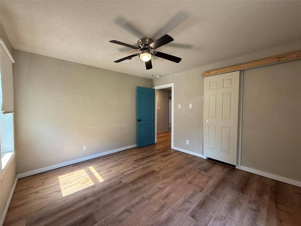 2703 Downing Avenue, Dallas, TX 75216 Room featuring wood-finish flooring, a ceiling fan with integrated light fixture, a blue paneled interior door, and a sliding closet door with a decorative wood header