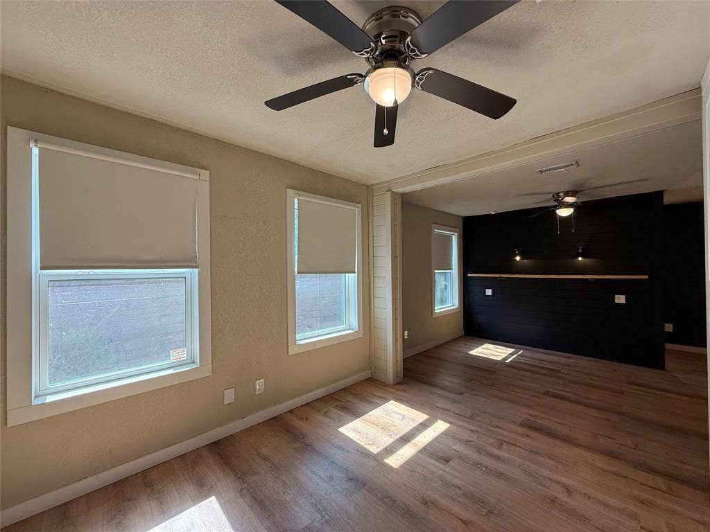 2703 Downing Avenue, Dallas, TX 75216 Wood-finish flooring, dark-toned accent wall, ceiling fans with integrated lighting, and neutral wall tones