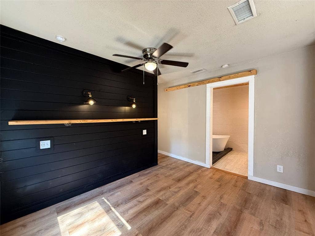 2703 Downing Avenue, Dallas, TX 75216 Black shiplap accent wall with built-in wood shelving and dual wall-mounted light fixtures, wood-finish flooring, ceiling fan, and natural wood barn door hardware