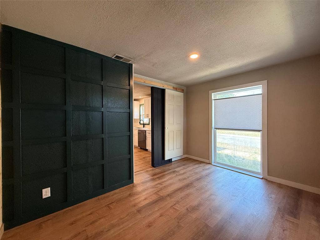 2703 Downing Avenue, Dallas, TX 75216 Interior space featuring grid-patterned dark accent wall, wood-finish flooring, sliding barn-style door, and large window with cellular shade