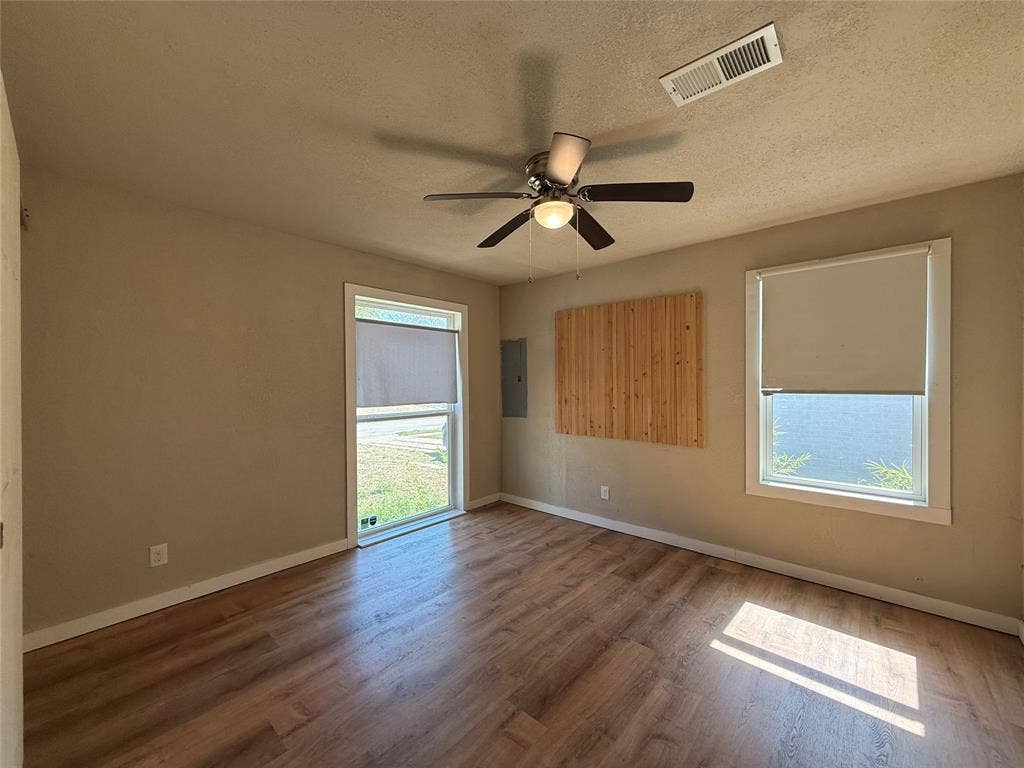 2703 Downing Avenue, Dallas, TX 75216 Room featuring wood-finish flooring, two windows with roller shades, and a ceiling fan with integrated lighting