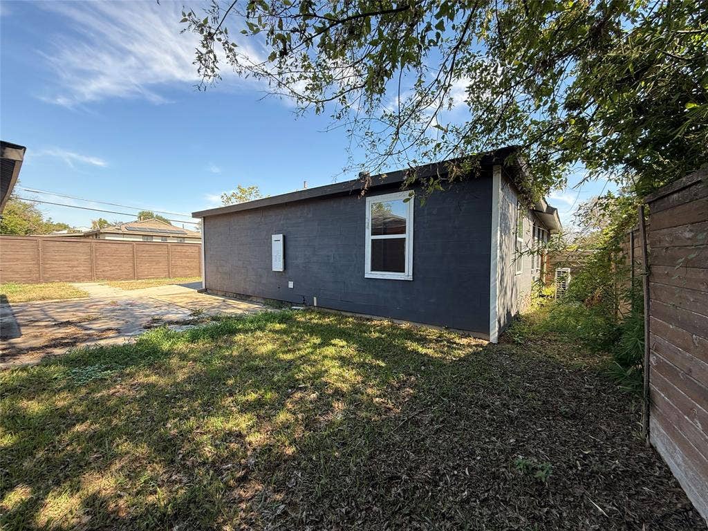 2703 Downing Avenue, Dallas, TX 75216 Exterior of the residence featuring painted masonry siding, a single-hung window, and a paved hardscape area enclosed by perimeter fencing