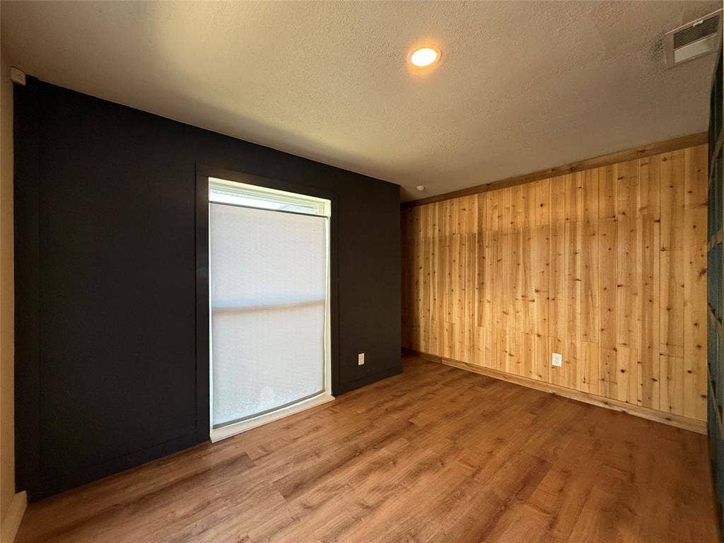 2703 Downing Avenue, Dallas, TX 75216 Room featuring wood-finish flooring, vertical natural wood paneling, contrasting dark-toned wall, and recessed lighting