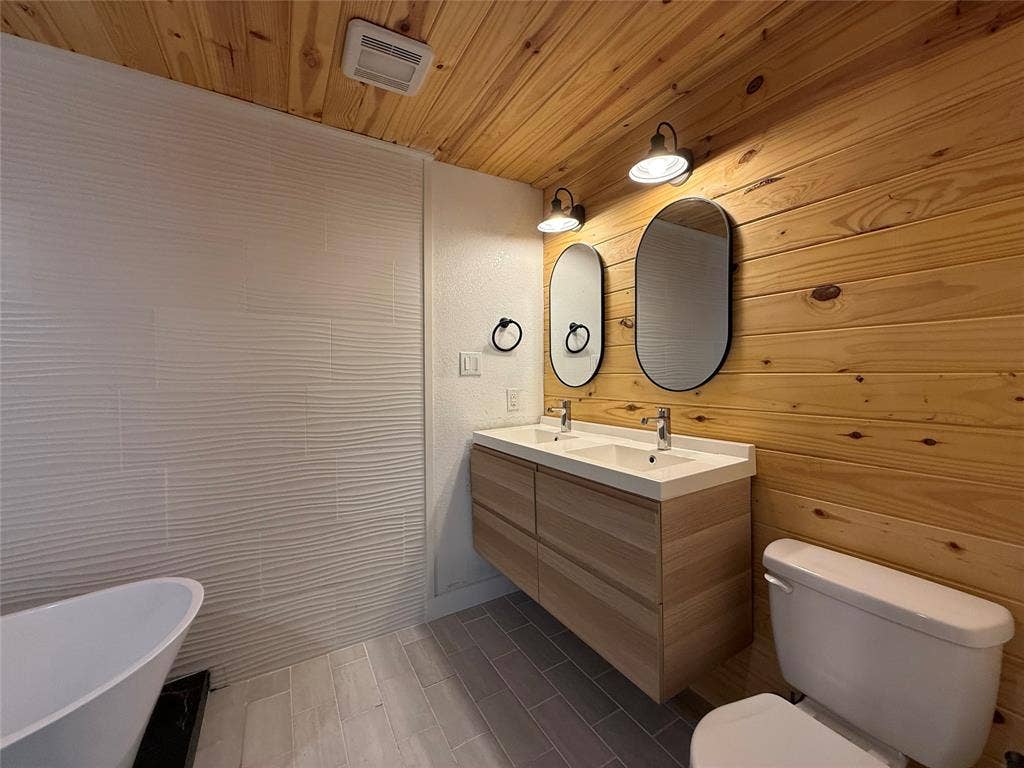 2703 Downing Avenue, Dallas, TX 75216 Floating dual-sink vanity with a solid-surface countertop, wood-paneled walls and ceiling, textured wall tile, and a freestanding soaking tub
