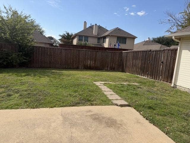 11159 Covey Lane, Frisco, TX 75035 Rear exterior area featuring a concrete patio, stone paver pathway, grass yard, and full-height wood privacy fencing