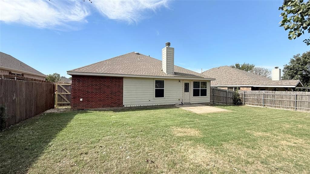 Backyard featuring a grass lawn, paved patio, red brick and horizontal siding exterior, masonry chimney, and wood privacy fencing