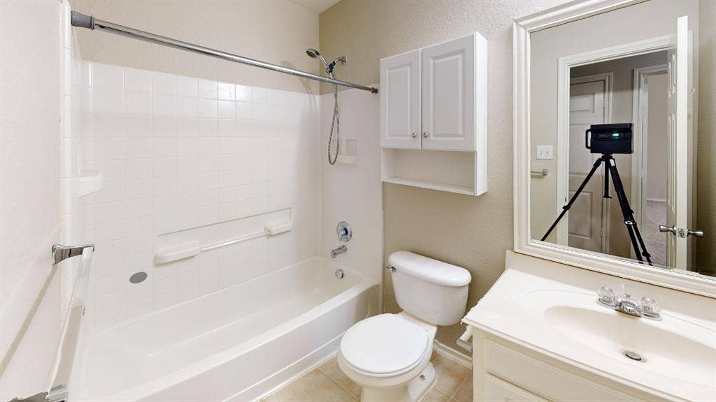 Bathroom featuring a tub and shower combination, wall-mounted storage cabinetry, a vanity with an integrated basin, and a framed mirror