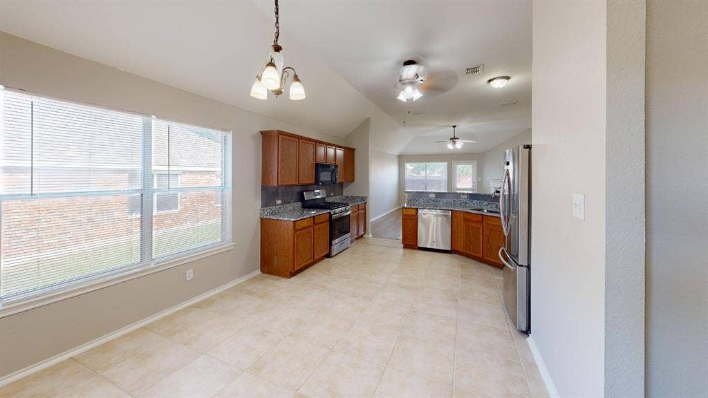 Kitchen featuring wood cabinetry, stone-finish countertops, stainless steel appliances, tile flooring, and vaulted ceilings