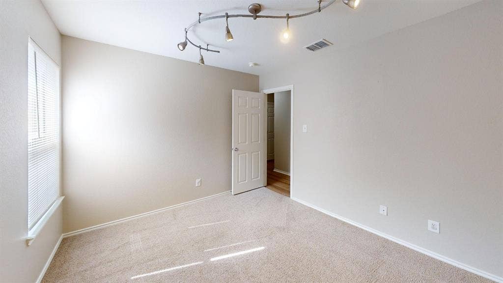 Neutral-toned interior featuring wall-to-wall carpeting, a multi-light track lighting fixture, and a single-panel interior door
