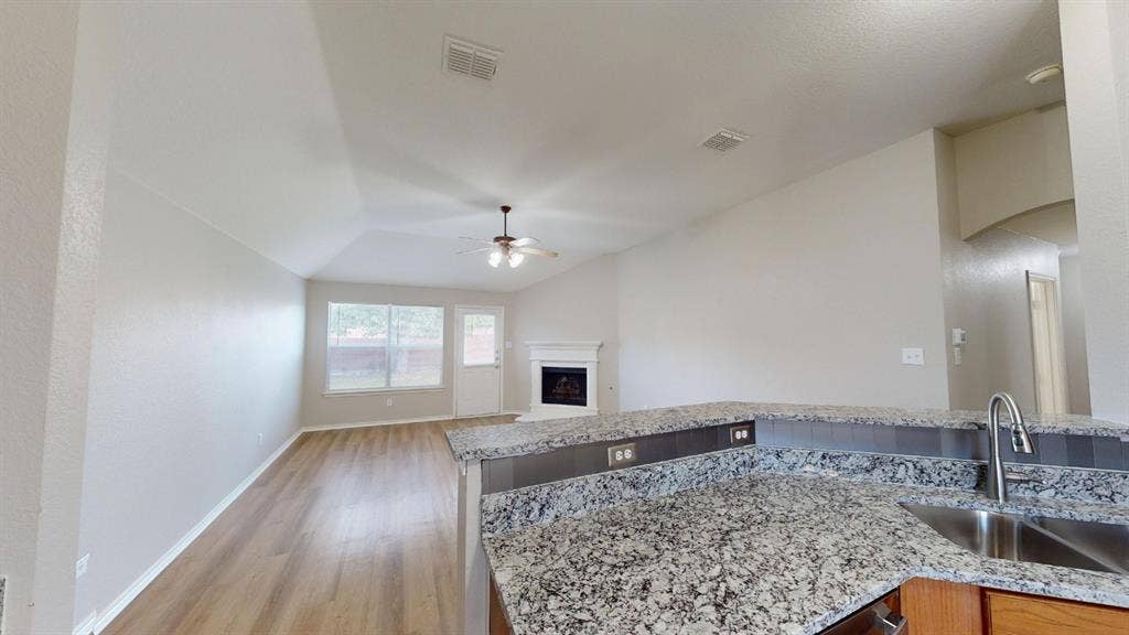 Kitchen featuring a stone-composite countertop, stainless steel sink with a high-arch faucet, vaulted ceilings, wood-finish flooring, and a fireplace with a white mantel