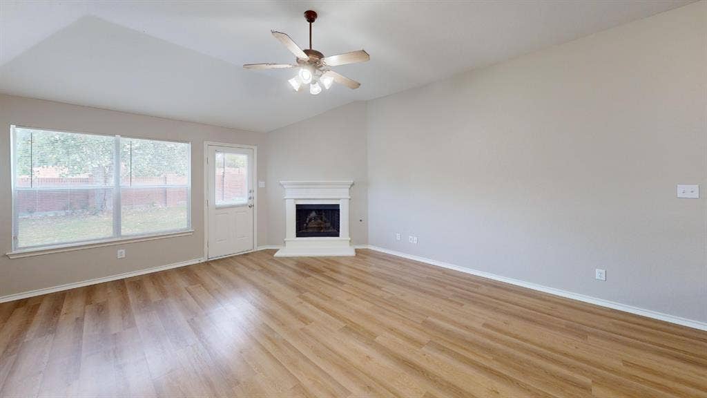 Vaulted ceilings, wood-finish flooring, corner fireplace with white mantle, ceiling fan with light fixture, and large windows