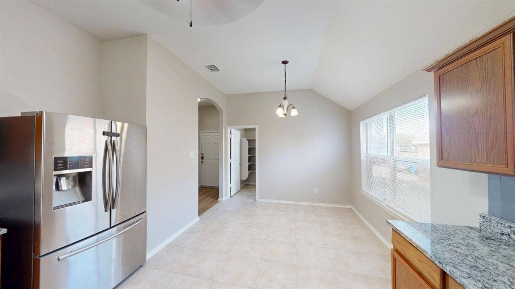 Kitchen area featuring vaulted ceilings, stainless steel refrigerator, stone-surfaced countertops, wood cabinetry, and neutral tile flooring
