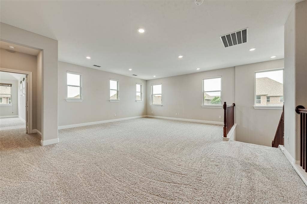 9829 Sharps Drive, Frisco, TX 75035 Expansive interior room featuring neutral wall tones, recessed lighting, wall-to-wall carpeting, multiple windows, and a wood-finish staircase railing