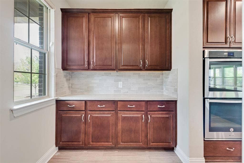 9829 Sharps Drive, Frisco, TX 75035 Custom cabinetry with dark wood finish, light-toned countertop, stacked tile backsplash, and built-in stainless steel double wall ovens