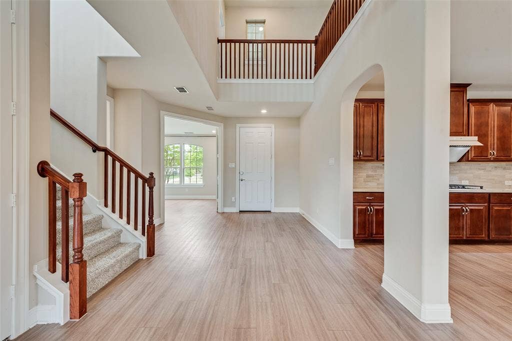9829 Sharps Drive, Frisco, TX 75035 Two-story foyer featuring wood-finish flooring, a wood-railed staircase, arched architectural detailing, and custom stained-wood cabinetry