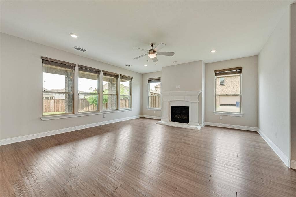 9829 Sharps Drive, Frisco, TX 75035 Open interior featuring wood-finish flooring, a white hearth fireplace, recessed lighting, a ceiling fan, and large windows with horizontal blinds