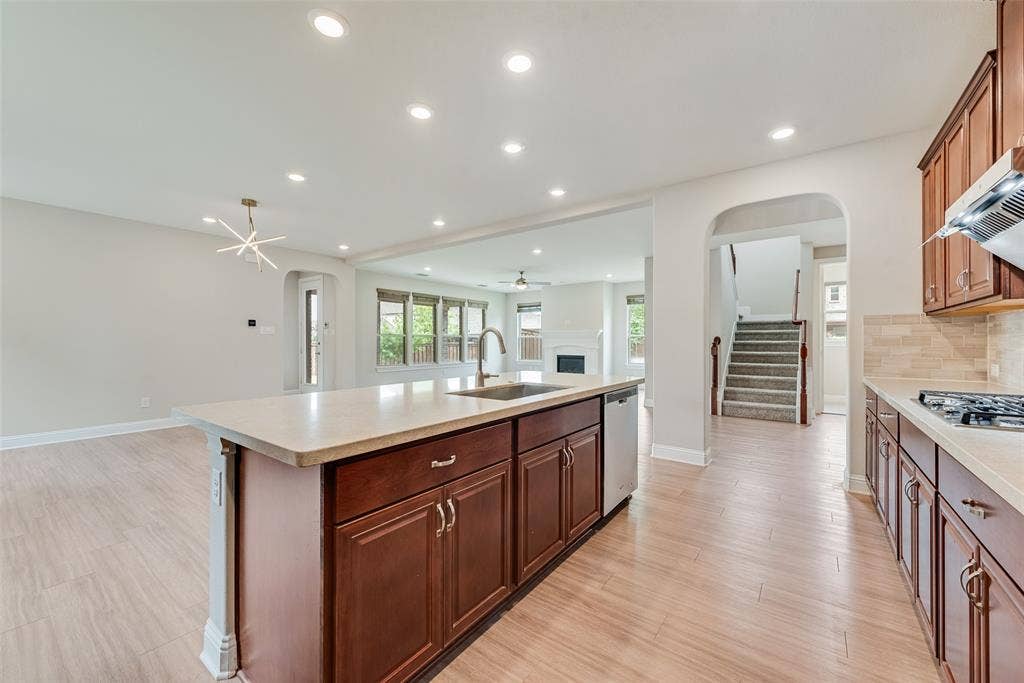 9829 Sharps Drive, Frisco, TX 75035 Kitchen featuring wood-finish cabinetry, a central island with an integrated stainless steel sink, recessed lighting, and tile flooring