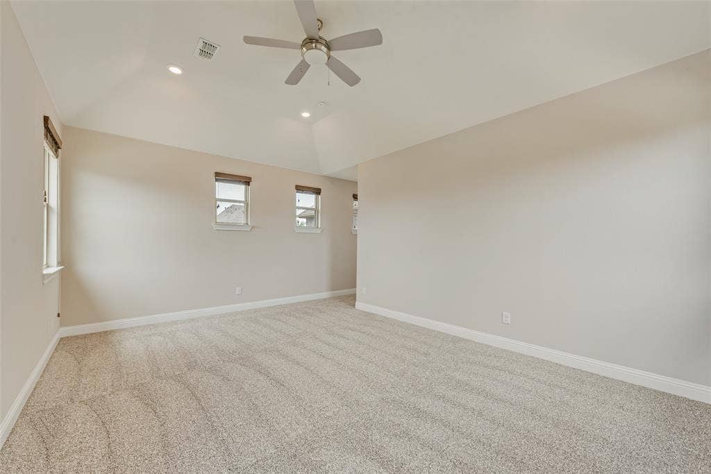 9829 Sharps Drive, Frisco, TX 75035 Vaulted ceilings, neutral wall color, plush wall-to-wall carpeting, multiple windows with neutral roller shades, and a ceiling-mounted fan with integrated lighting
