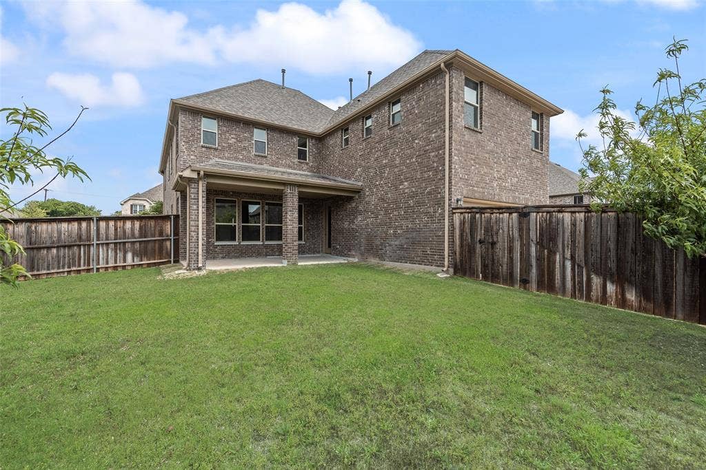 9829 Sharps Drive, Frisco, TX 75035 Two-story brick exterior featuring a covered patio, shingle roof, and full wood privacy fencing
