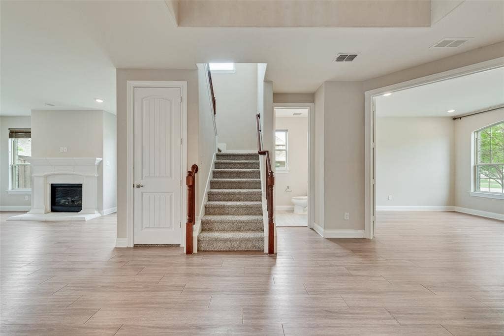 9829 Sharps Drive, Frisco, TX 75035 Interior space featuring wood-finish flooring, a white-mantel fireplace, a central staircase with a wood handrail, and arched doorways
