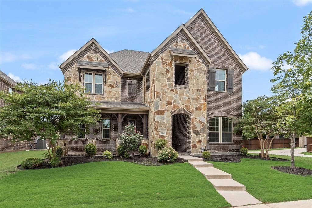 9829 Sharps Drive, Frisco, TX 75035 Two-story traditional exterior featuring a blend of multi-toned stone and brick masonry, covered front porch, decorative wood-finish shutters, and gabled roofline