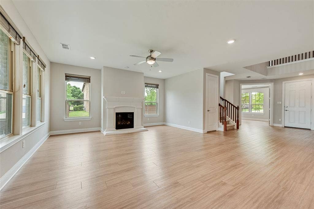 9829 Sharps Drive, Frisco, TX 75035 Open-concept interior featuring wood-finish flooring, a white mantel fireplace, recessed lighting, a ceiling fan, and staircase with wooden handrails