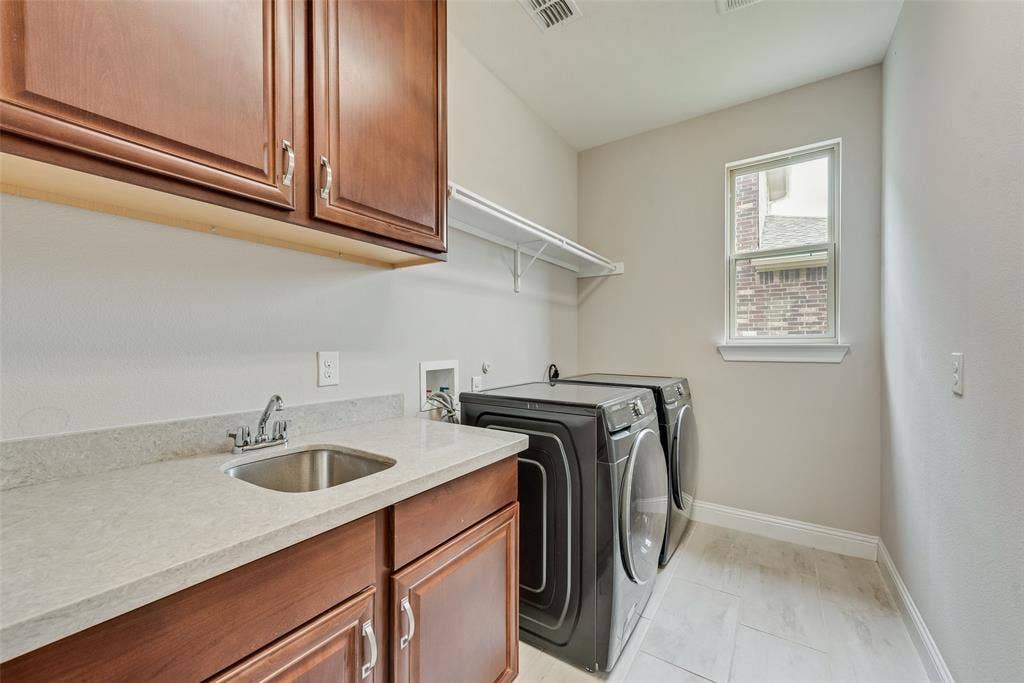 9829 Sharps Drive, Frisco, TX 75035 Laundry area featuring wood-finish cabinetry, solid-surface countertop, stainless steel drop-in sink with chrome faucet, and white tile flooring