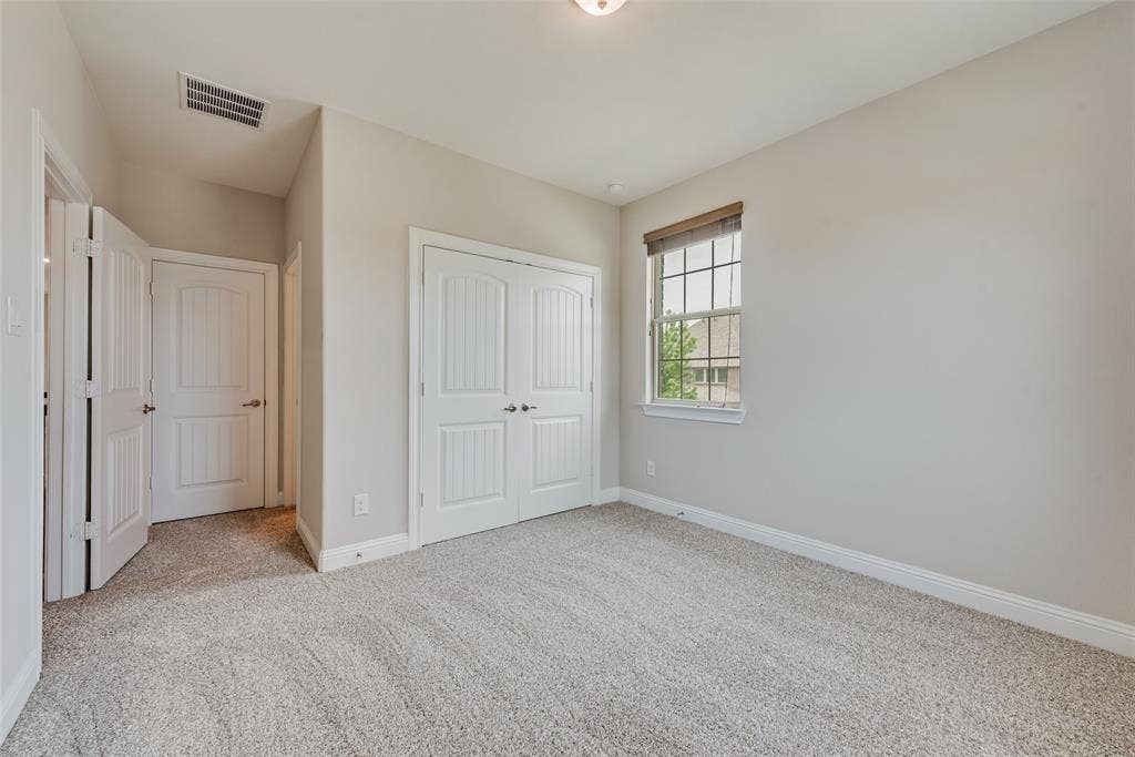 9829 Sharps Drive, Frisco, TX 75035 Neutral-toned interior room featuring wall-to-wall carpeting, dual-panel closet doors, a single-hung window with a wooden valance, and a flush-mount ceiling light fixture
