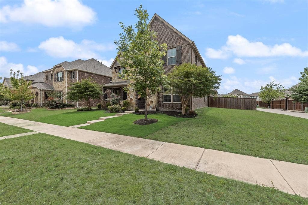 9829 Sharps Drive, Frisco, TX 75035 Multi-story brick exterior featuring steep roof pitches, decorative shutters, a covered entryway, and a landscaped lawn