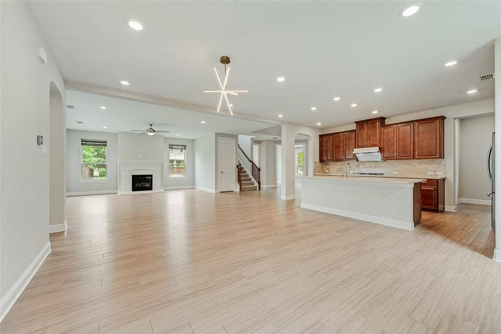 9829 Sharps Drive, Frisco, TX 75035 Open floor plan featuring wood-finish flooring, recessed lighting, a fireplace with a decorative mantel, a central island kitchen with wood cabinetry, and a geometric chandelier