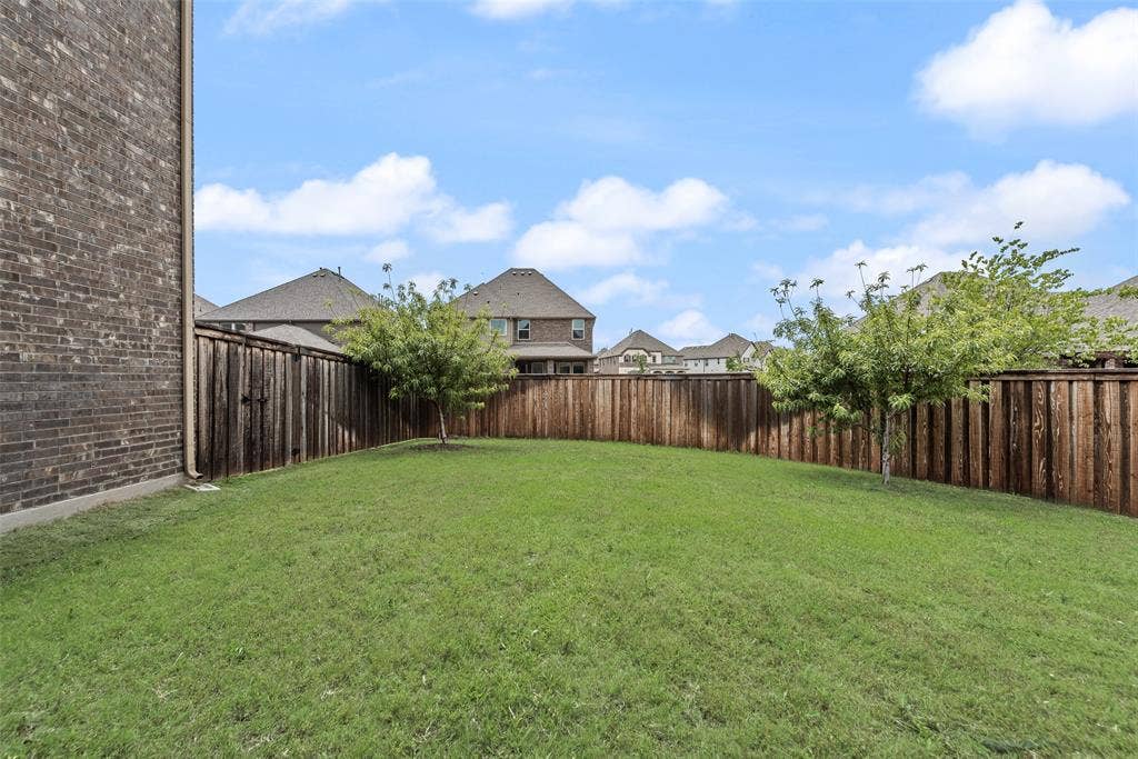 9829 Sharps Drive, Frisco, TX 75035 Private backyard featuring a brick exterior wall, manicured grass lawn, wood privacy fencing, and two mature trees