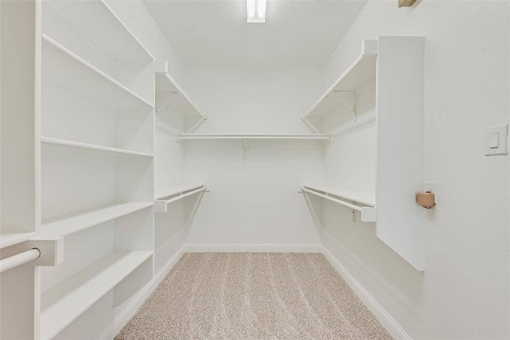 9829 Sharps Drive, Frisco, TX 75035 Walk-in closet featuring white built-in shelving, integrated hanging rods, and neutral carpeting