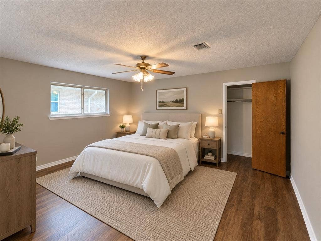 Bedroom featuring wood-finish flooring, a multi-blade ceiling fan with integrated light fixture, a wide window, and a built-in closet with a solid wood-finish door