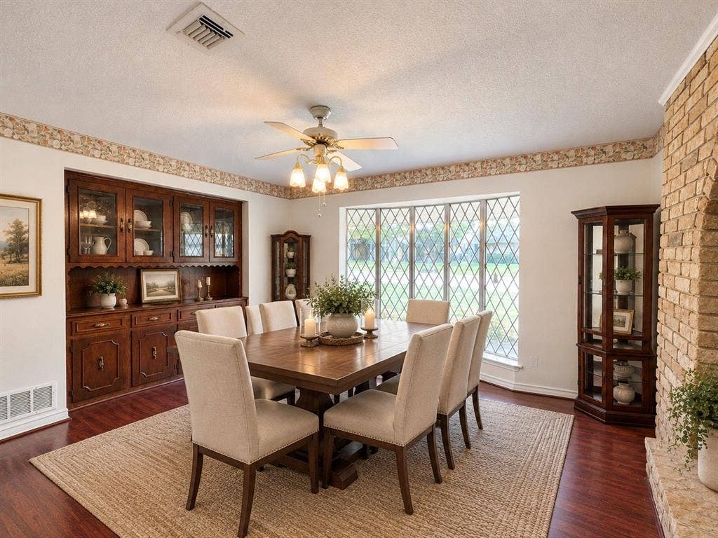 Dining area featuring dark wood-finish flooring, built-in stained wood cabinetry, floor-to-ceiling diamond-pane window, and textured light-toned brick fireplace surround